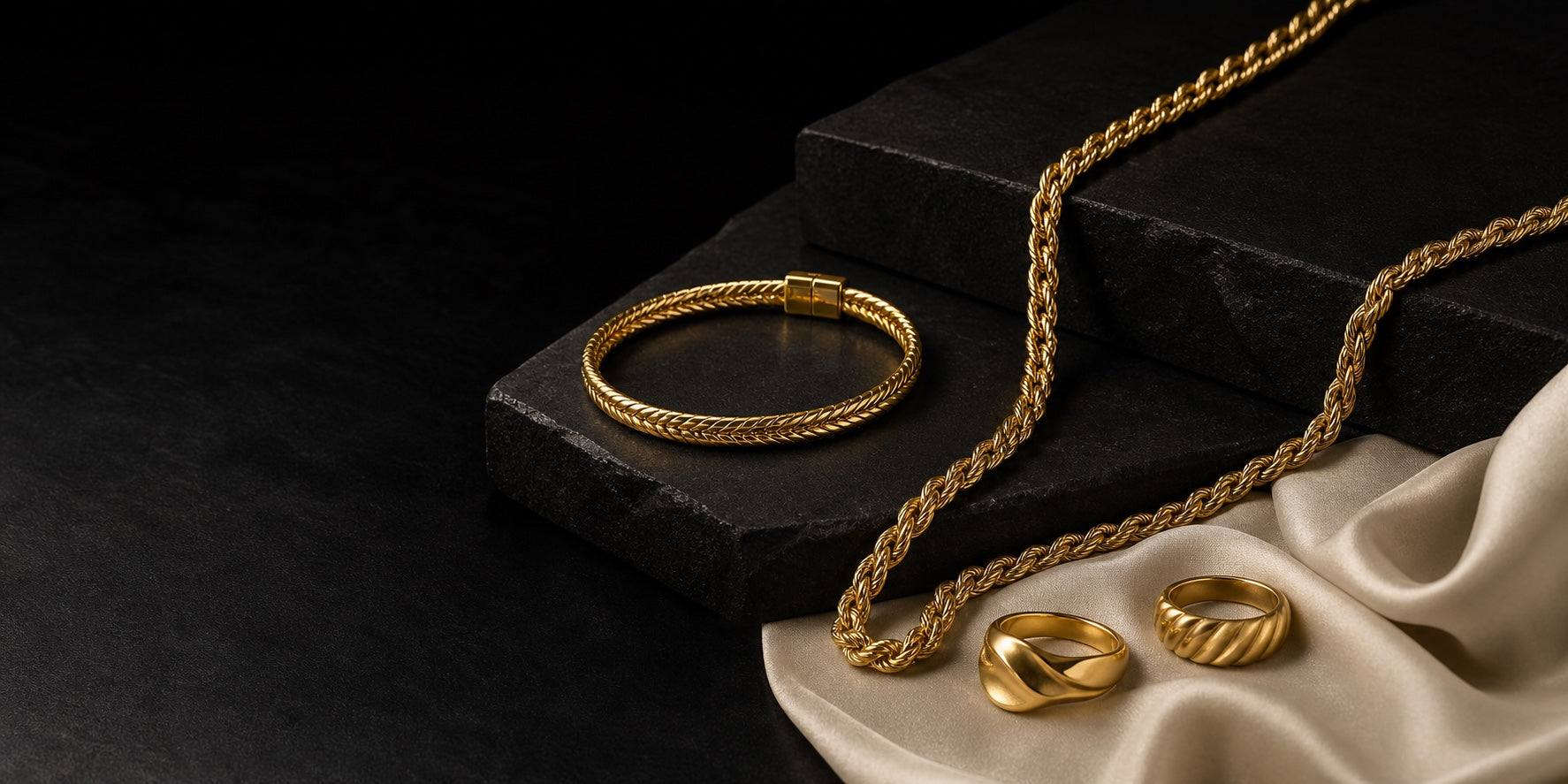 Gold jewelry arranged on black stone and ivory silk
