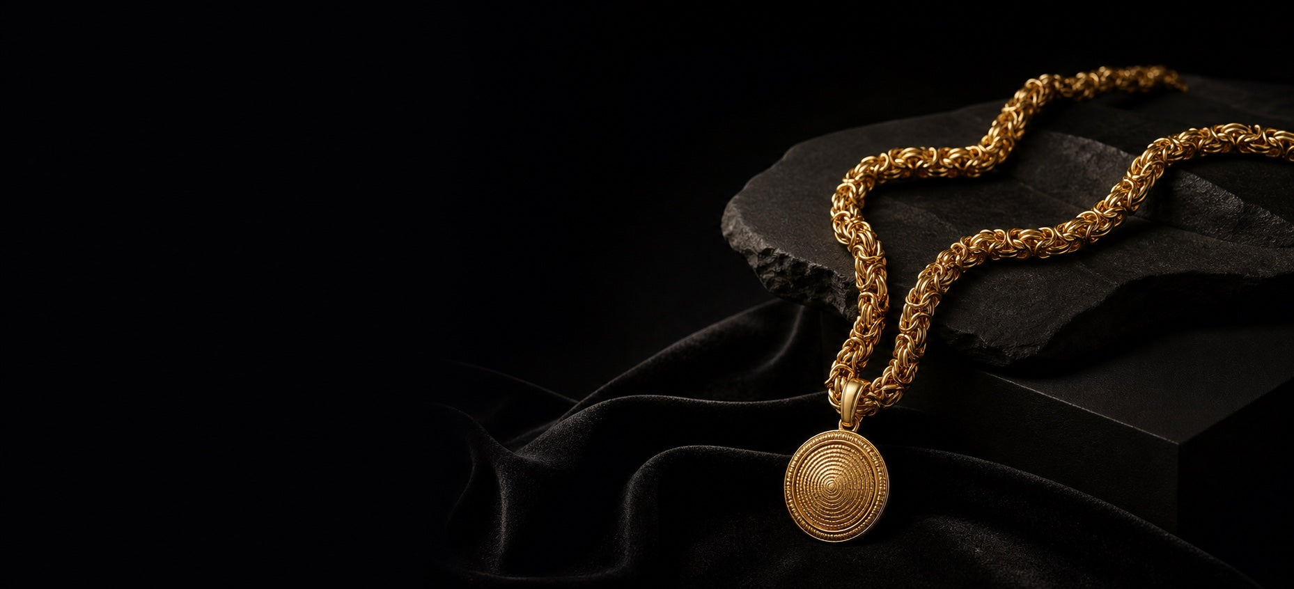 Gold chain and pendant arranged on matte black stone